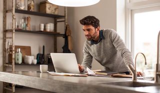 효율적인 원격 작업을 위해 LED 작업 조명이 설치된 밝은 홈 업무 공간에서 노트북을 사용하는 남자.
